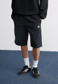 Black athletic shorts made of soft fabric, featuring an elastic waistband and side pockets. Notable white Adidas logo and flat hem.