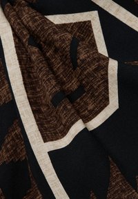 Stoff mit einem geometrischen Muster in Dunkelbraun, Creme und Schwarz. Die Textur wirkt gewebt mit einer weichen, glatten Oberfläche.