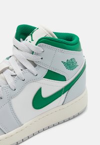 Szare skórzane sneakersy z zielonymi akcentami, białymi sznurowadłami i wyściełanym kołnierzem. Posiadają logo Air Jordan oraz zakrzywiony swoosh Nike z boku.