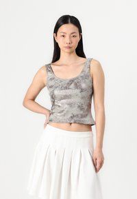 Fémes ezüst színű rövid top sima textúrával, széles pántokkal és lekerekített nyakkivágással, fehér, pliszírozott szoknyával párosítva.