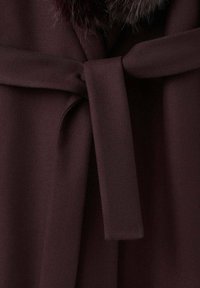 Bordeauxrode stof met een gestructureerde weef, voorzien van een gebonden ceintuur in de taille en een imitatiebonten kraag voor extra detail.