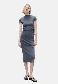 Robe midi ajustée grise avec des manches courtes et un col haut. Le tissu est lisse et extensible. Assortie à des sandales plates noires et un bracelet en argent.