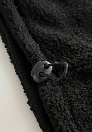 Fleece negru cu o textură și un sistem de prindere cu cordon. Materialul este moale și are un model în bucle pe margine.