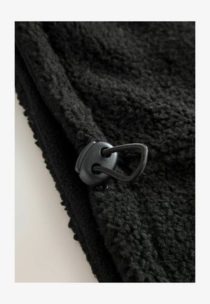 Fekete bolyhos anyag, texturált felülettel és fűzőzsinórral. Az anyag puha, és hurkos minta fut végig a szélén.