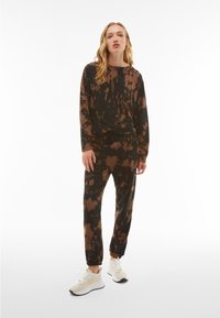 Black and brown tie-dye loungewear set featuring a long-sleeve top and elasticized jogger pants, made from soft fabric with a relaxed fit.