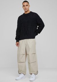 Pull en tricot noir avec motifs texturés, associé à un pantalon cargo beige avec de grandes poches et des baskets blanches.