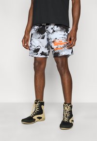 Κοντό παντελόνι με γκρι και μαύρο μοτίβο και πορτοκαλί λογότυπο, συνδυασμένο με ψηλά αθλητικά παπούτσια σε μαύρο και κρεμ χρώμα. Απλός σχεδιασμός, ελαφρύ ύφασμα.