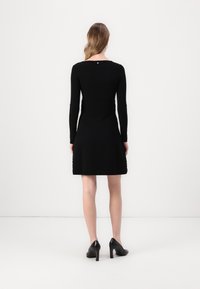 Black long-sleeve dress with a fitted bodice and flared skirt; textured detailing near the hem, rounded neckline, and a back button closure.