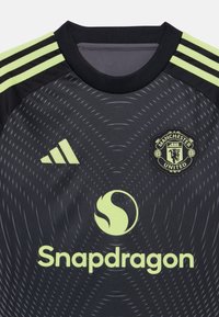 Maillot de sport noir avec des accents vert fluo. Comprend le logo Adidas, le blason de Manchester United et la marque Snapdragon. Design texturé avec des lignes.