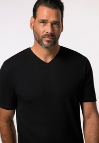 T-shirt nera a maniche corte in tessuto a costine con design a V. Il materiale appare liscio con una silhouette aderente.