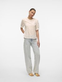 Floral print blouse in light beige, round neckline, short puff sleeves; paired with light blue wide-leg jeans and yellow heeled sandals.