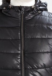 Zwarte pufferjas met een glanzende buitenkant, horizontaal doorgestikt ontwerp, ritssluiting en verstelbare trekkoorden bij de capuchon.