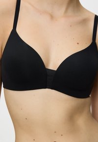 Reggiseno nero in un tessuto morbido e liscio; presenta un design senza cuciture a scollatura profonda, spalline regolabili e una fascia larga per il supporto.