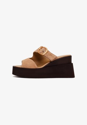 Sandalia beige de ante con plataforma, suela negra gruesa, punta abierta y tira con hebilla dorada en la parte superior.