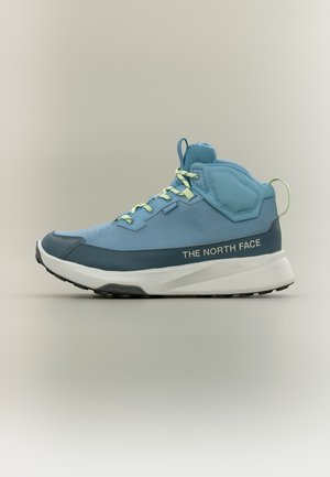 Niebiesko-turkusowy wysokiej jakości but trekkingowy z białą podeszwą, jasnozielonymi sznurowadłami i logo "The North Face" po boku.