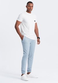 Valkoinen lyhythihainen t-paita rintataskulla, yhdistettynä vaaleansinisiin collegehousuihin. Mallilla on päällään valkoiset tennarit. Yksinkertainen ja rento muotoilu.