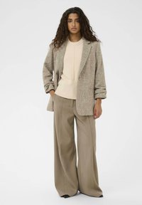 Bež blazer iz volnenega mešanega materiala z teksturirano zaključkom, s spuščenimi rokavi in enim gumbom, v kombinaciji z svetlim širokima hlačami.