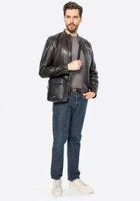 Giubbotto di pelle nera con chiusura a zip, indossato sopra una maglietta grigia. Jeans blu e sneaker bianche completano l'outfit, accompagnato da una borsa a tracolla nera.