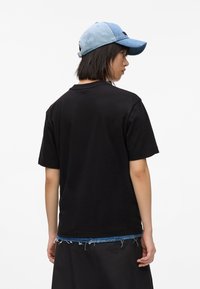 Tricou negru din bumbac, cu mâneci scurte, purtat sub o fustă neagră. O șapcă din denim albastru, cu vizieră curbată, completează ținuta.