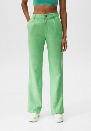 Vrouw draagt lichtgroene wijde broek met hoge taille, groen cropped top en wit-groene sneakers, staat met handen in de zakken.