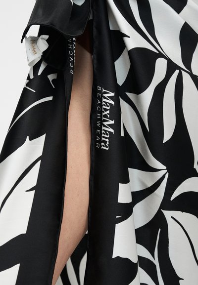 Υφασμα με ασπρόμαυρο σχέδιο φύλλων και το κείμενο "MaxMara Beachwear" που καλύπτει μερικώς γυμνό δέρμα.