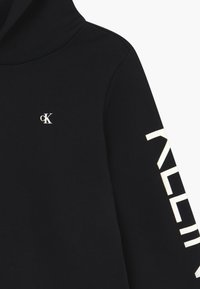 Sudadera negra de algodón suave, con un pequeño logo blanco "ck" en el pecho y el texto "CALVIN" impreso en blanco a lo largo de la manga.