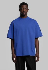 T-shirt bleu surdimensionné à manches courtes, fabriqu�é en coton doux, avec un col rond côtelé et une petite étiquette noire sur la manche gauche.