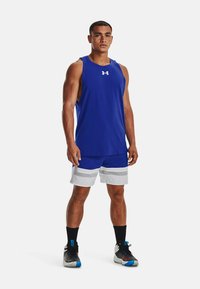Blaues ärmelloses Sport-Tanktop, kombiniert mit grauen und blauen Shorts mit horizontalen Streifen und schwarzen Laufschuhen mit bunten Akzenten.