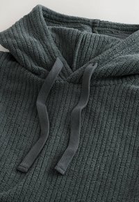 Felpa verde scuro con un tessuto a coste texture, caratterizzata da un collo a V, lacci e un interno morbido e peloso.