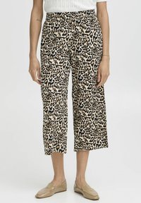 Kalhoty s leopardím potiskem, zkrácené, s elastickým pasem. Materiál vypadá lehký a hladký, s béžovým pozadím a černými a hnědými skvrnami.