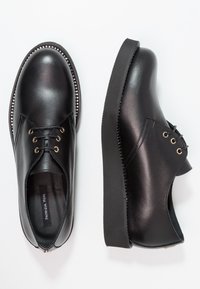 Scarpe in pelle nera con lacci, punta rotonda, superiore testurizzato, occhielli dorati e suola nera spessa con cuciture decorative lungo il bordo.