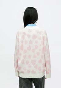 Džemperis no adītas auduma ar baltu pamatu un rozā sirdis rakstu. Raksturo brīvs piegriezums, ribots aproces un apaļa kakla izgriezums.