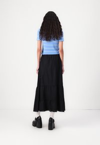Top a maniche corte a righe blu e bianche abbinato a una gonna nera a balze di lunghezza alla caviglia. Il modello indossa scarpe con platform nere.