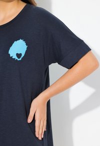 Marinblå T-shirt i mjukt material, med en turkos hjärtgrafik på bröstet och uppvikta korta ärmar.