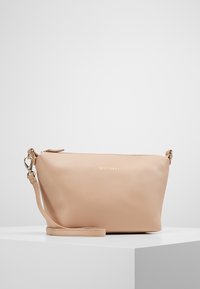 Beige texturerad lädervristväska med guldzipper och liten guld logotyp på framsidan, placerad på vit yta mot en enkel bakgrund.