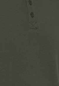 Oliven grøn bomulds polo-shirt med en tekstureret overflade, tre knaplukninger og forstærket syning under kraven.