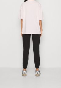 Ljusrosa välfitad bomullströja i lös stil, kombinerad med svarta joggarbyxor. Outfiten fulländas med svarta och vita sneakers.