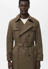 Bruine, dubbelgeknoopte trenchcoat met een riem, uitgerust met een kraag, schouderepauletten en klepzakken. Gemaakt van een gladde, duurzame stof.