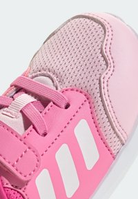 Różowy but sportowy z siateczkową cholewką i akcentami z syntetycznej skóry. Charakterystyczne detale to białe paski z logo i sznurowadła.