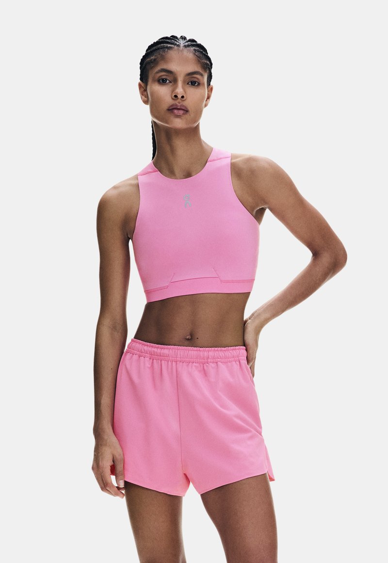 Femme aux cheveux tressés portant un crop top rose sans manches et un short rose à taille élastique, debout avec une main sur la hanche.