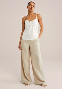 White, sleeveless top with textured fabric and floral embroidery; paired with light beige, wide-leg pants in a smooth fabric.