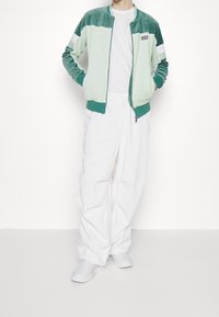 Kurtka typu bomber z aksamitu w miętowym kolorze z białymi akcentami, połączona z luźnymi białymi spodniami i białymi trampkami. Casualowy, luźny krój.