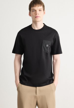 Black short-sleeve T-shirt featuring a textured chest pocket with a logo patch. Soft fabric with a relaxed fit and round neckline.