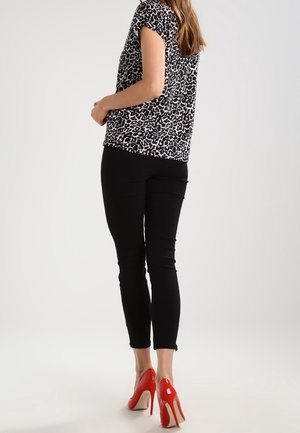 Top de leopardo en blanco y negro de manga corta, combinado con pantalones negros ajustados y zapatos de tacón rojo. Textura de tela suave.