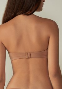 Strapless, naadloze bruine bandeau top met een gladde textuur en een haak-en-oogsluiting op de rug, ontworpen voor comfort en minimale zichtbaarheid.