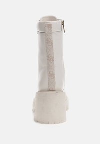 Botín blanco hasta el tobillo con un tacón alto y grueso, parte trasera reforzada y una correa decorativa crema con patrones de logotipo. Cierre de cremallera en el lado.