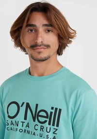 Mėtų žalios spalvos ilgomis rankovėmis marškinėliai su ryškiu juodu logotipu "O'Neill SANTA CRUZ CALIFORNIA-U.S.A." Minkšta medvilnės medžiaga su apvalia iškirpte.