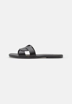 Black slide sandal with crisscross strap design, flat sole, matte texture, and minimalistic profile. Suitable for casual wear.