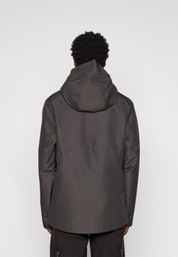 Tmavošedá kapucňová bunda so hladkou textúrou, s predĺženým lemom a jednoduchým, funkčným dizajnom. Pohľad zozadu zvýrazňuje tvar kapucne.