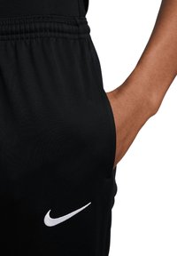 Pantaloni sportivi neri con vita elasticizzata e tasche laterali; presenta un logo Nike bianco sulla parte bassa della gamba. Tessuto liscio e leggero.
